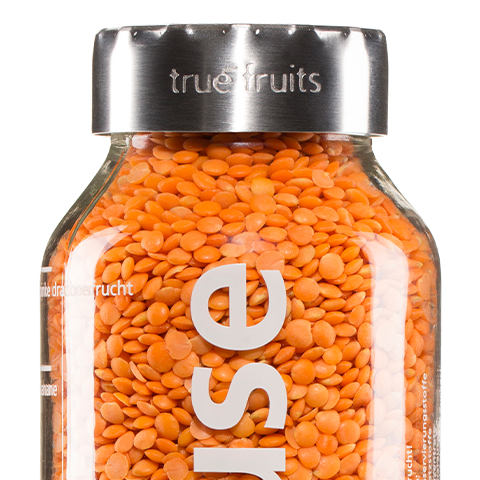 true fruits - Upcycling true fruits Flasche mit Flaschenaufsatz, gefüllt mit Linsen vor weißem Hintergrund